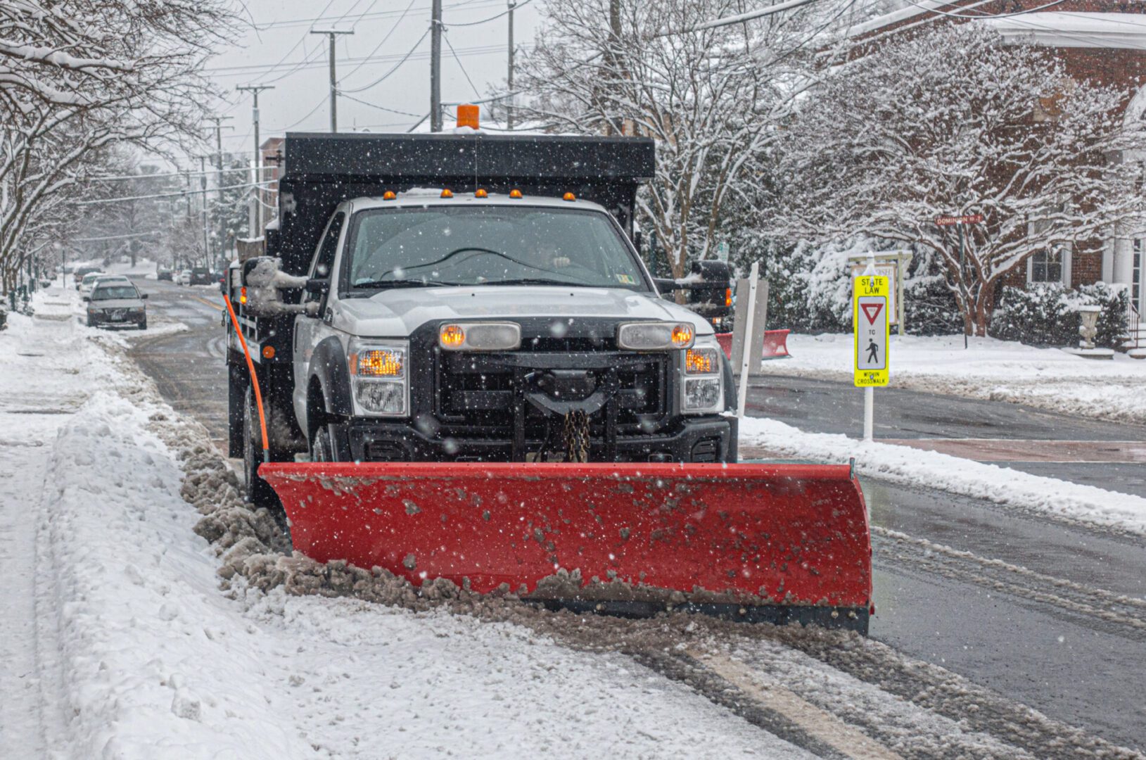 Snowplow clearing snow-covered urban street.