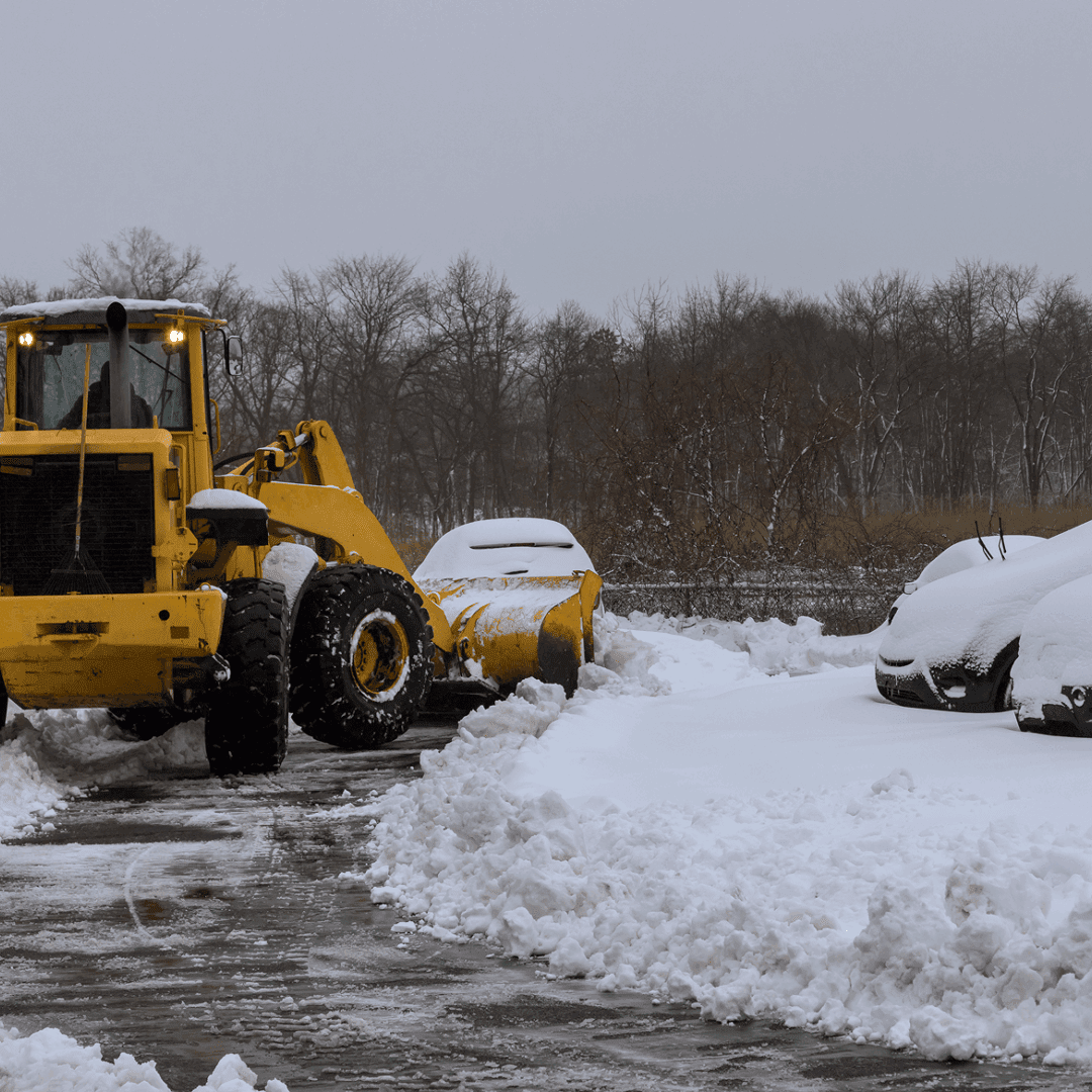 Snowplow clearing snow-covered parking lot.